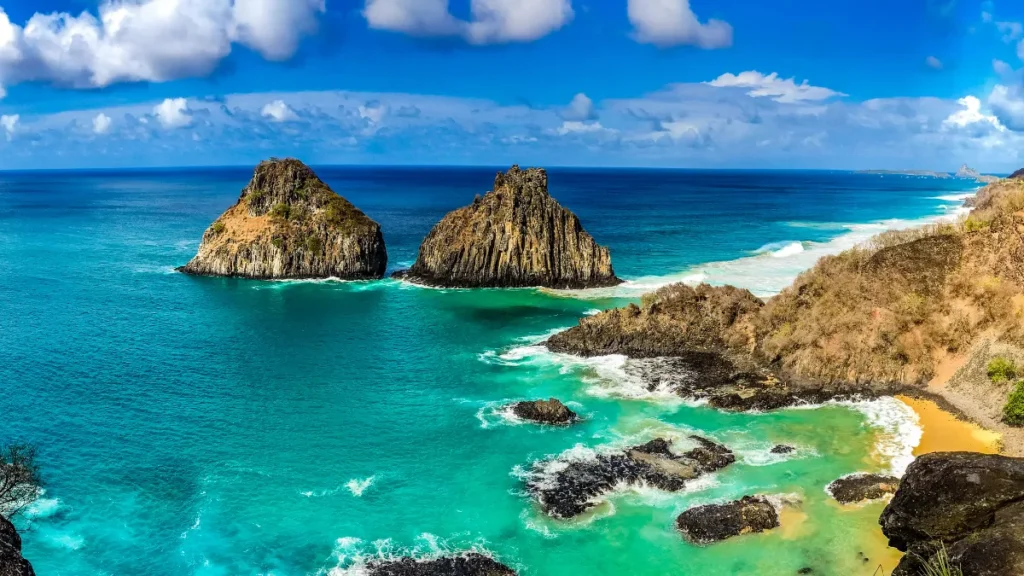 Vista aérea da Praia do Sancho em Fernando de Noronha com embarcações no mar cristalino.